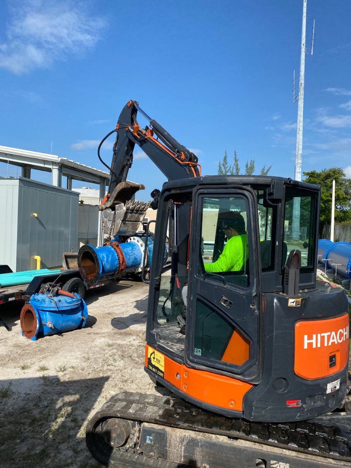 Operador de RCR en miniexcavadora junto a tubería azul de gran diámetro