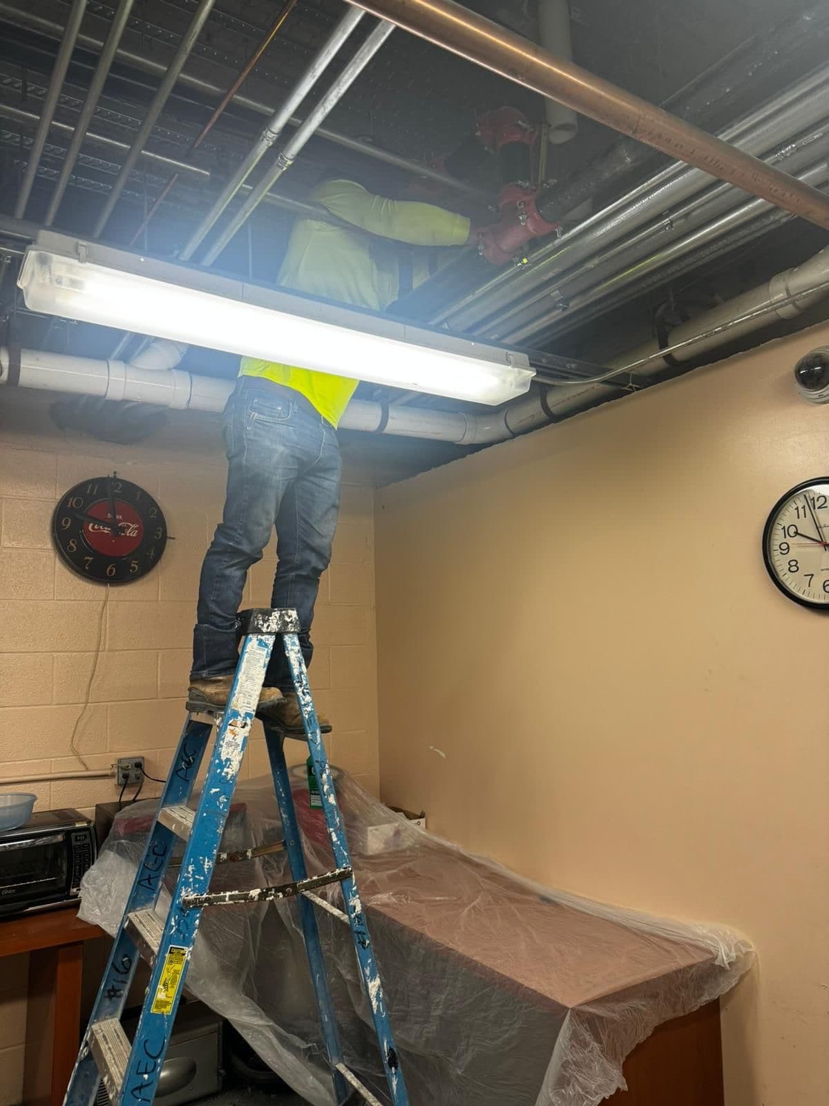 Plomero de RCR en escalera trabajando sobre el cielorraso de una oficina