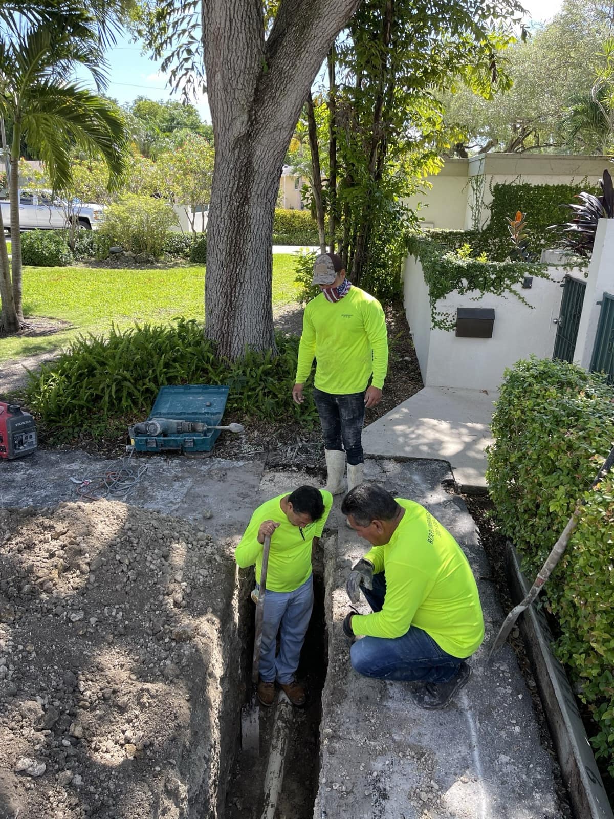 Cuadrilla de RCR con camisetas fosforito trabajando en una zanja frente a una casa