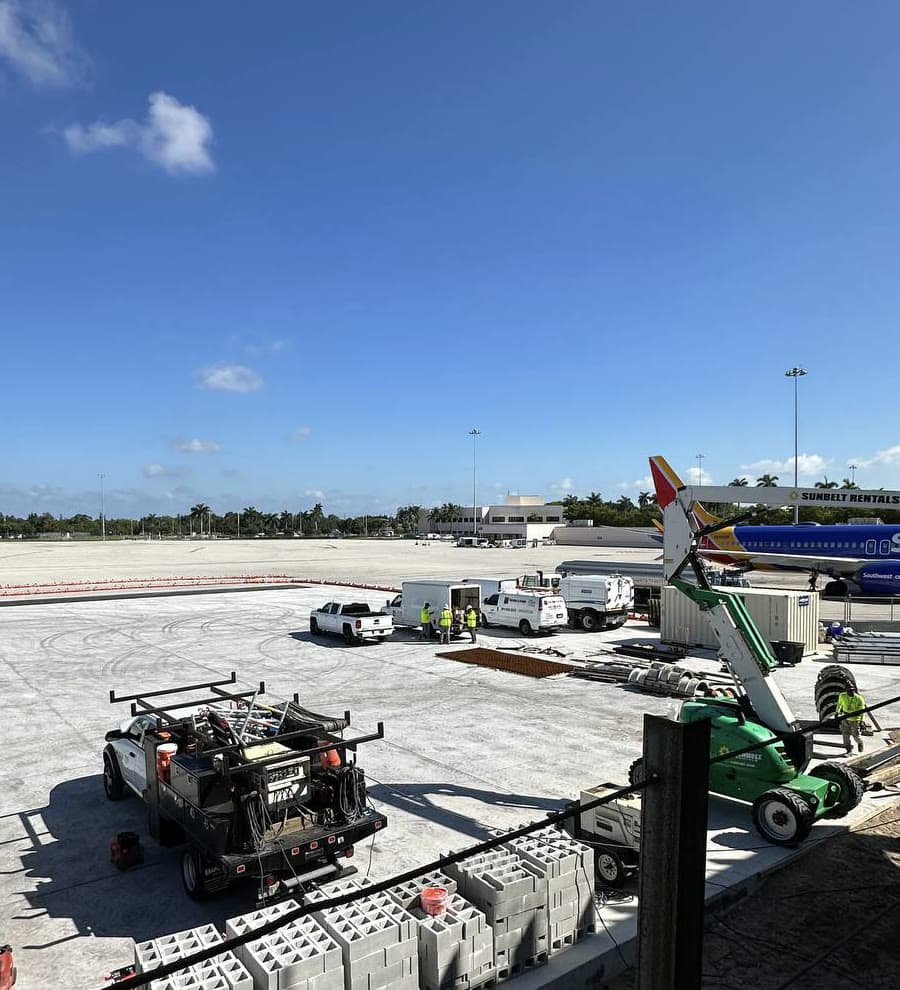 Vista de la plataforma del aeropuerto de Palm Beach con camionetas de obra y un avión de Southwest al fondo
