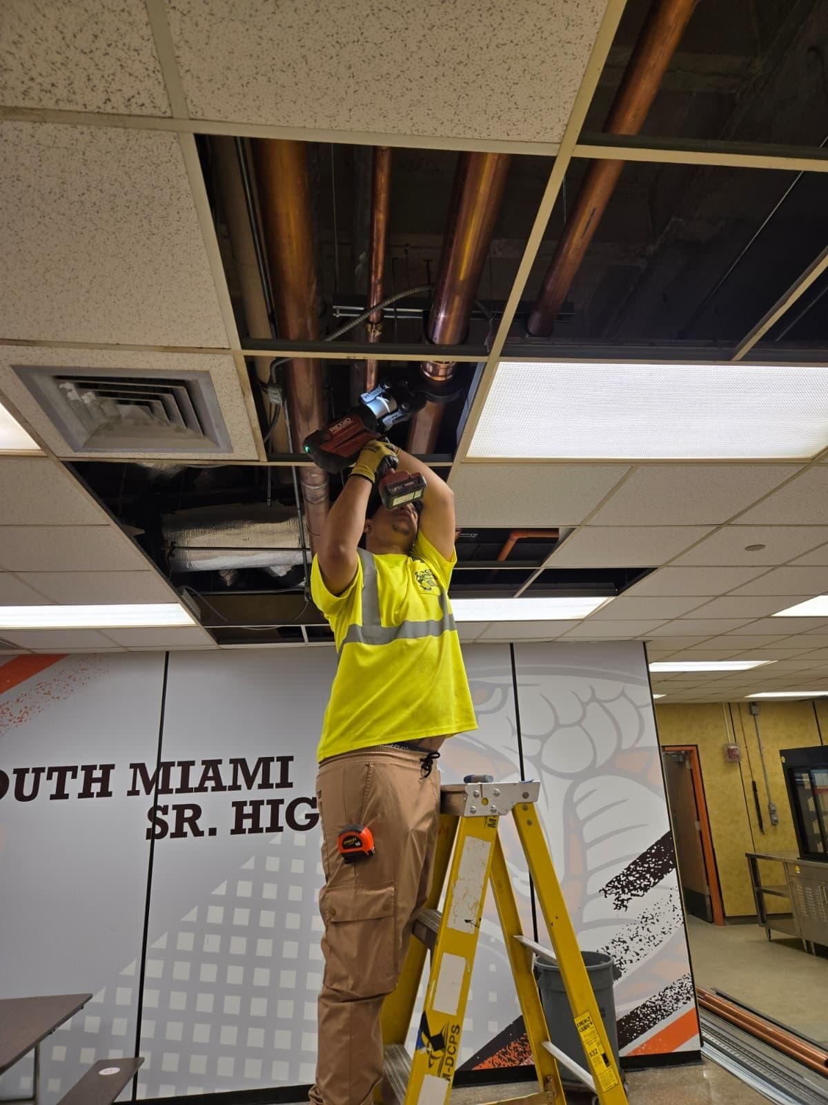 Plomero de RCR en escalera trabajando en el cielorraso de South Miami Senior High
